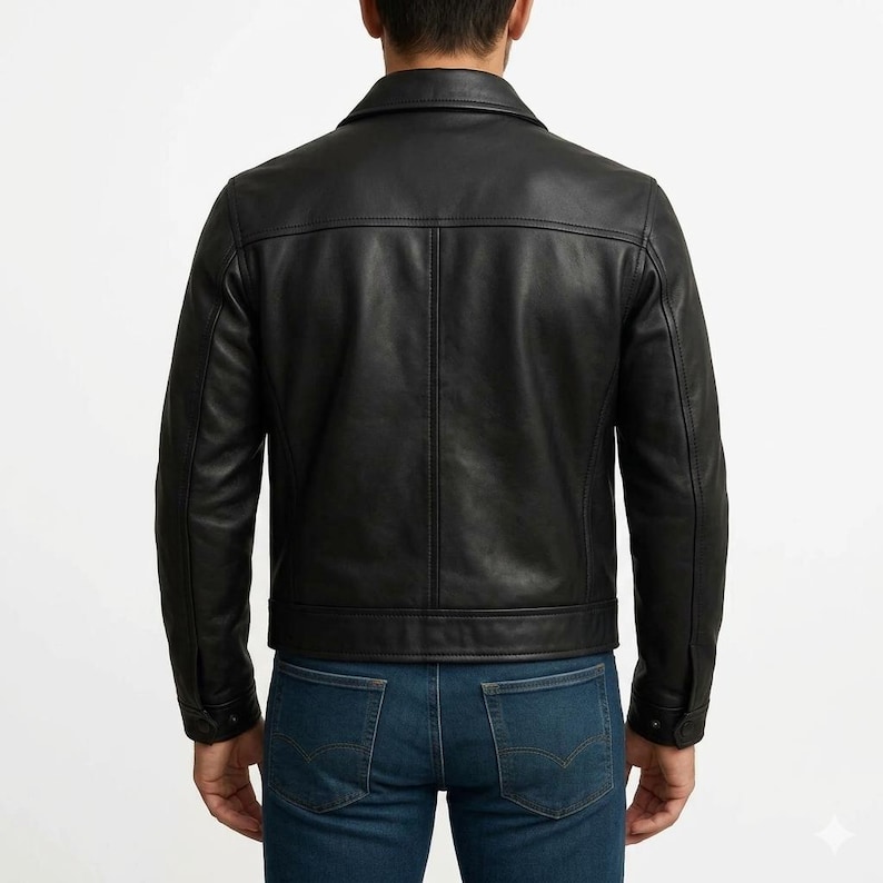 May include: A black leather jacket with a classic design. The jacket features a collared neckline, buttoned cuffs, and a straight hem. The back view shows the jacket's tailored fit and stitching details. The model is wearing blue jeans.