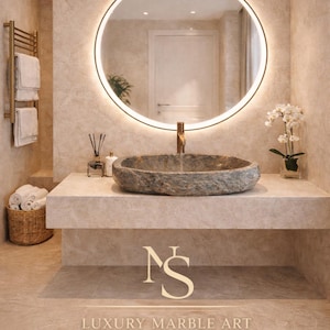 Puede incluir: Un baño moderno con un lavabo de piedra, un grifo dorado y un espejo redondo iluminado. Un toallero dorado y una cesta de mimbre con toallas están a la izquierda. Las palabras "LUXURY MARBLE ART" están en la parte inferior.