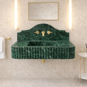 May include: A luxurious bathroom vanity with a green marble sink and gold fixtures. A white towel hangs on a gold towel rack. A small side table with a marble top and gold legs is next to the sink. A mirror hangs above the sink.