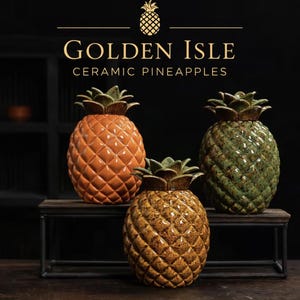 Puede incluir: Tres esculturas de piña de cerámica en tonos naranja, verde y amarillo-marrón. Las piñas tienen superficies texturizadas y copas verdes y frondosas. El texto "GOLDEN ISLE CERAMIC PINEAPPLES" se muestra encima de las esculturas.