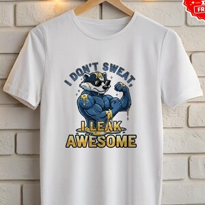 May include: White t-shirt featuring a cartoon badger flexing its muscles, wearing sunglasses, and the text "I DON'T SWEAT, I LEAK AWESOME" in blue and yellow. The shirt is hanging on a wooden hanger.