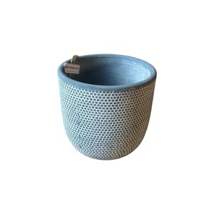 Puede incluir: Una maceta cilíndrica con un acabado azul mate y un patrón de rejilla blanco texturizado que cubre el exterior. El borde es de color azul sólido y una pequeña etiqueta rectangular con el texto WWW.TOFFINO.DE está unida al borde interior.