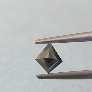 May include: A dark gray, square-cut gemstone is held by tweezers against a light blue background. The gemstone has a faceted surface, reflecting light. The shape is a symmetrical, four-sided diamond cut, showcasing its geometric precision. This image highlights the gemstone's color and clarity.