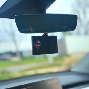 Peut inclure: Accessoire de voiture noir avec le mot «ANNUAL» sur un emblème rouge et blanc, suspendu au rétroviseur d'une voiture. L'accessoire est rectangulaire et comporte un graphique de montagne et d'arbre.