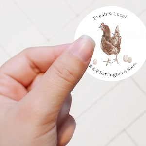 May include: A round white sticker featuring a watercolour illustration of a brown chicken standing between two small eggs. The text Fresh & Local is printed in black above the chicken, and R & E Darlington & Sons. is printed below the chicken.