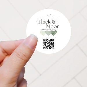 May include: A circular white sticker featuring the black text Flock & Moor, the words PERSONALISED GIFTS, three watercolor-style hearts in shades of green, and a black square QR code centered at the bottom of the sticker design.