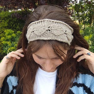 Peut inclure: Un bandeau tricoté de couleur beige présentant un motif répétitif en forme de feuilles avec des détails ajourés. L'accessoire est réalisé avec un fil texturé et possède un bord tressé sur le haut et le bas, offrant un aspect uniforme.