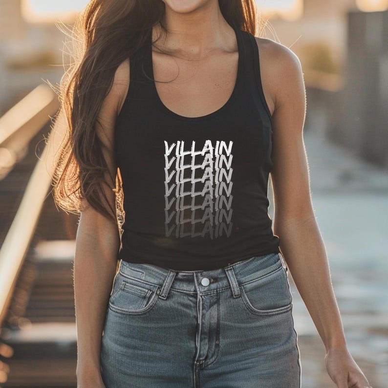May include: Black vest top featuring the word "VILLAIN" in a stacked, white and grey gradient design. The top is worn with blue denim jeans. The image is well-lit, highlighting the casual style.