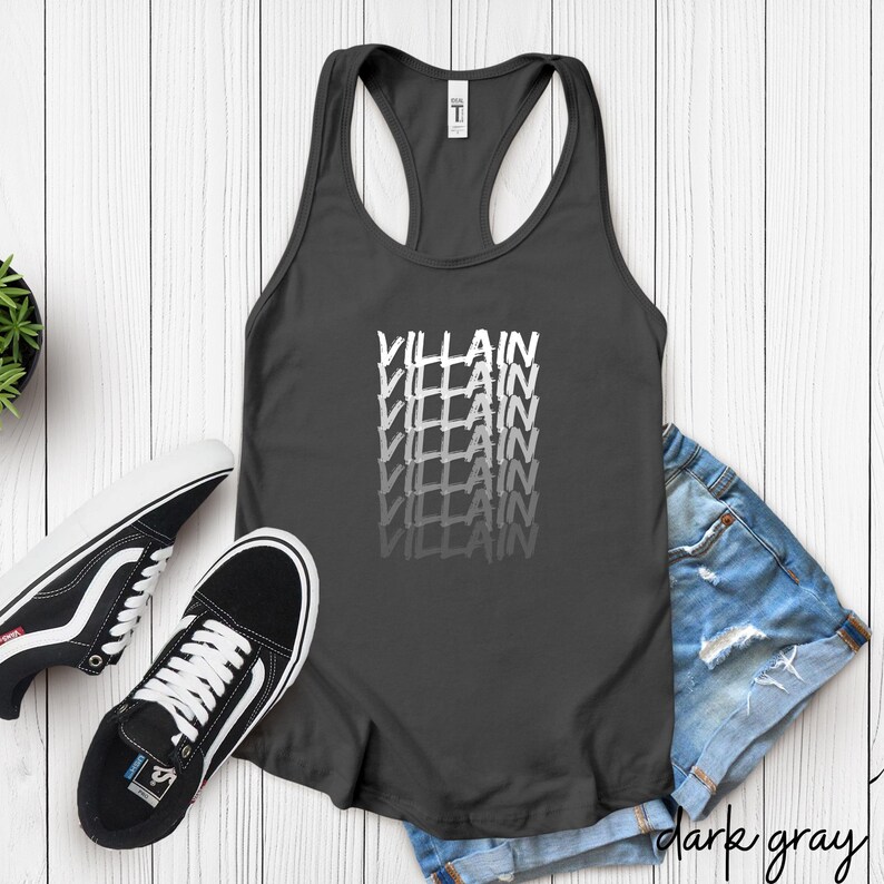 May include: Dark grey vest top featuring the word "VILLAIN" stacked vertically in a white, slightly blurred font. The top is styled with black and white trainers and denim shorts.