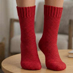May include: A pair of bright red knitted socks. The socks are knee-high with a ribbed cuff and a textured knit pattern. The socks are displayed on a wooden table.
