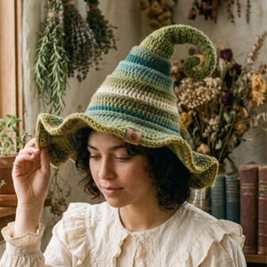 May include: A crocheted hat featuring a tall, curled point and a wide, wavy brim. The hat is crafted with horizontal stripes in various shades of green, teal, and white, and includes a small, rectangular brown leather-like tag on the brim.