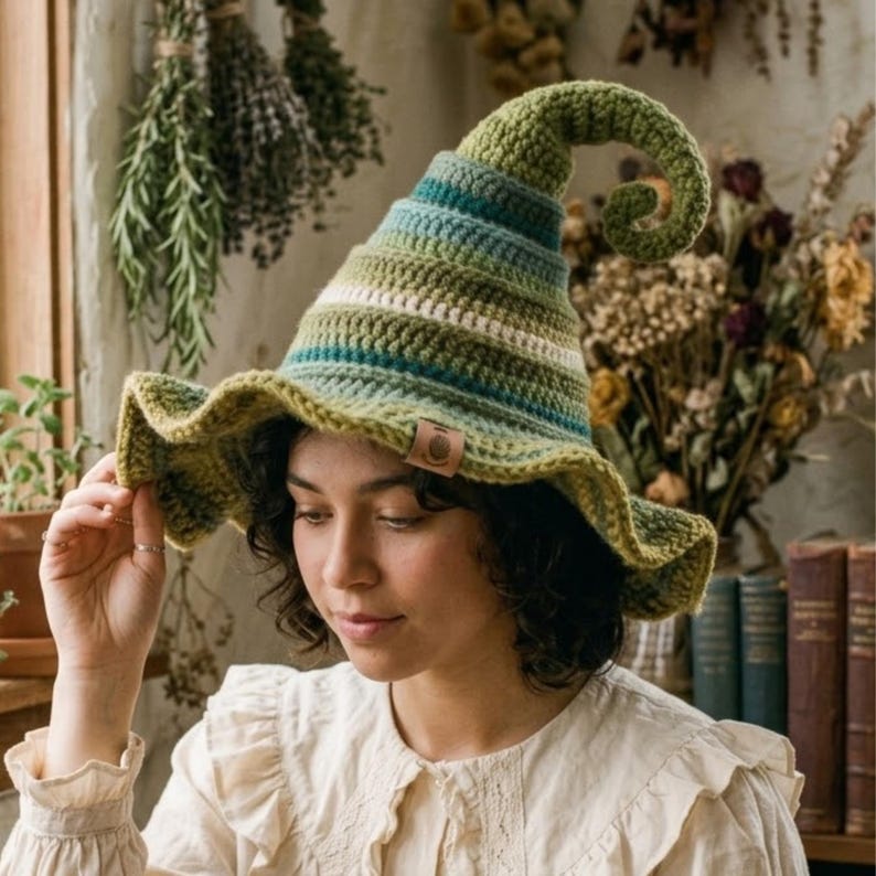 May include: A crocheted hat featuring a tall, curled point and a wide, wavy brim. The hat is crafted with horizontal stripes in various shades of green, teal, and white, and includes a small, rectangular brown leather-like tag on the brim.