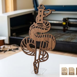 Può includere: Un ritaglio di legno marrone a forma di serpente con un faro in cima. Il serpente presenta dettagli intagliati. Il design è esposto su un supporto trasparente, con icone di file DXF, SVG, PDF e PNG nell'angolo.