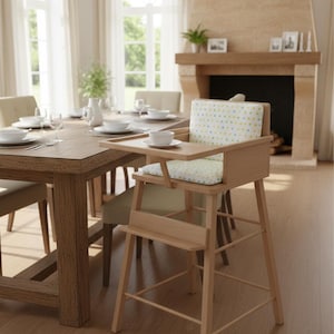 May include: A wooden high chair with a tray and a patterned cushion. The chair is light brown and has a footrest. The background shows a dining table set for a meal, with a fireplace and windows.