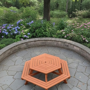 Könnte beinhalten: Ein orangefarbener, sechseckiger Picknicktisch und ein passender kleinerer Tisch auf einer Steinterrasse. Die Tische sind aus Holz und von üppigem Grün umgeben, darunter Bäume, Büsche und Blumen. Die Szene spielt sich im Freien ab.