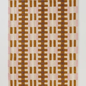 May include: A rectangular rug with a wavy edge, featuring a repeating pattern of brown, pink, and cream-colored rectangles. The rug has a textured, tufted appearance, creating a visually appealing design. The color palette is neutral with warm tones.
