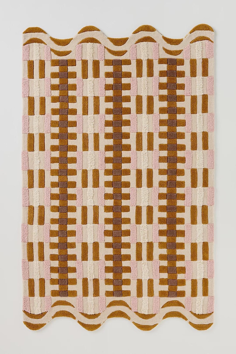May include: A rectangular rug with a wavy edge, featuring a repeating pattern of brown, pink, and cream-colored rectangles. The rug has a textured, tufted appearance, creating a visually appealing design. The color palette is neutral with warm tones.