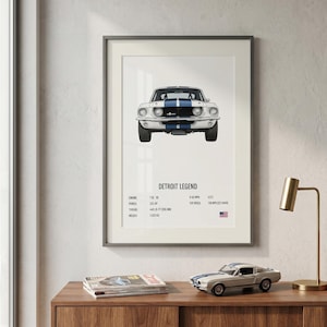 Op de afbeelding: Een ingelijste print van een witte en blauwe klassieke auto, met de tekst "Detroit Legend". De print toont specificaties. Een modelauto staat op een houten oppervlak.