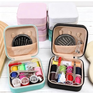 May include: A collection of small, zippered sewing kits in various colors, including pink, white, black, and teal. Each kit is open, revealing spools of thread, needles, scissors, and other sewing essentials. The kits are arranged on a light-colored surface.