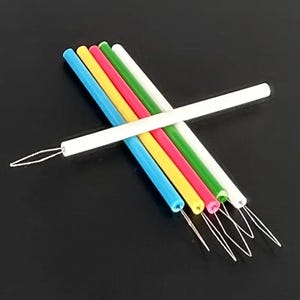 May include: A collection of colorful loop turners in blue, yellow, red, green, and white. Each turner has a colored handle and a white loop at the end. The tools are arranged diagonally against a black background.