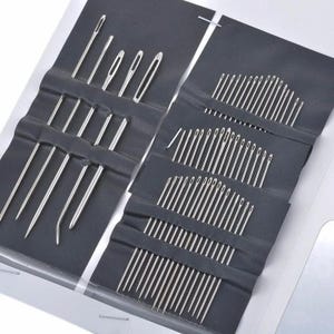 May include: A collection of sewing needles in various sizes, neatly arranged in a black fabric case. The needles are silver and have different eye sizes and lengths. The case is open, revealing multiple compartments filled with needles, ideal for sewing and crafting projects.