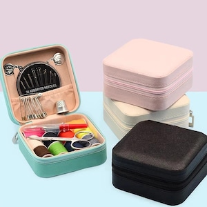 May include: A teal sewing kit with assorted needles, safety pins, and spools of thread. The kit is open, revealing its contents. Several zippered square cases in pink, cream, and black are stacked nearby, suggesting a collection of storage solutions.