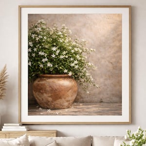 Peut inclure: Impression d'art encadrée d'un grand pot en terre cuite rempli de fleurs blanches en forme d'étoile et de feuilles vertes. Le pot est posé sur une surface en bois contre un mur texturé aux tons neutres, créant une esthétique naturelle.