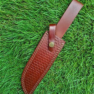 May include: A brown leather knife sheath with a woven texture and white stitching. The sheath has a brown leather belt loop and a button closure. The text "x - 624" is in the upper left corner.