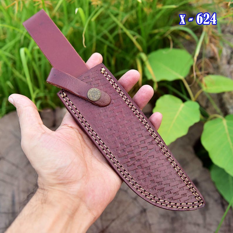 May include: A burgundy leather knife sheath with a woven texture and white stitching. The sheath has a strap with a button closure and a decorative metal button. The text "X - 624" is visible in the upper right corner.