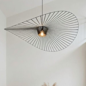 Puede incluir: Comedor moderno con una gran lámpara colgante de estructura de alambre negro. Debajo, una mesa rectangular con tapa de mármol está rodeada de sillas de madera con asientos tejidos. Un jarrón con flores secas está sobre la mesa.
