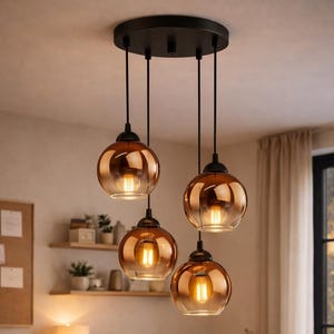 Puede incluir: Cuatro lámparas colgantes con pantallas esféricas de vidrio ámbar cuelgan de una lámpara de techo negra. Cada lámpara tiene una bombilla visible de tono cálido. Las luces están suspendidas sobre una mesa de madera, creando un ambiente cálido y acogedor.