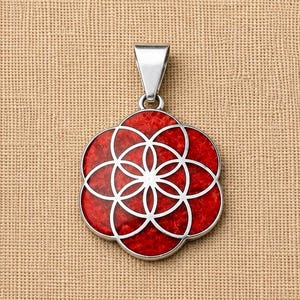 Puede incluir: Colgante plateado con un diseño floral rojo y blanco. El colgante tiene forma circular con un patrón de flores. El fondo es de tela beige.