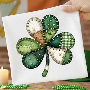 May include: A white square cloth with a patchwork shamrock design. The shamrock is made from various green fabrics, including solid, plaid, and textured patterns, stitched together with contrasting thread. A candle and green beads are in the background.