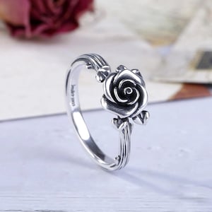 May include: A silver ring featuring a detailed rose design. The ring's band has a textured, ribbed pattern, and the rose is the focal point. The ring is likely made of sterling silver, with the inscription "India 925" visible on the band.