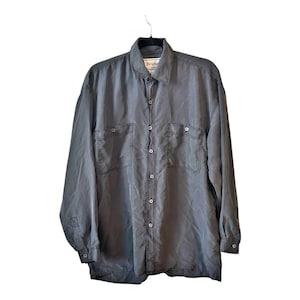 May include: A gray button-down shirt with long sleeves, two chest pockets, and a collar. The shirt is hanging on a black hanger. The brand name "Bruno" is visible on the collar.