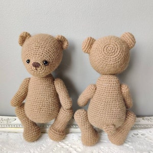 Pu&ograve; includere: Due orsacchiotti di peluche all'uncinetto, uno marrone e uno beige, sono seduti su un tovagliolo di pizzo bianco. Gli orsacchiotti hanno occhi e nasi marroni e sono rivolti in direzioni diverse.
