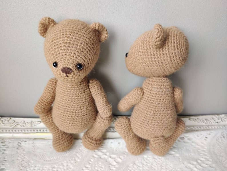 Pu&ograve; includere: Due orsacchiotti di peluche all'uncinetto, uno marrone e uno beige, in piedi su una superficie di pizzo bianco. Gli orsacchiotti hanno occhi neri e nasi marroni.