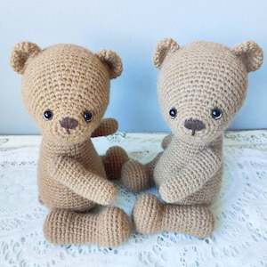 Pu&ograve; includere: Due orsacchiotti di peluche color marrone in crochet con occhi neri e nasi marroni seduti su un tovagliolo di pizzo bianco.