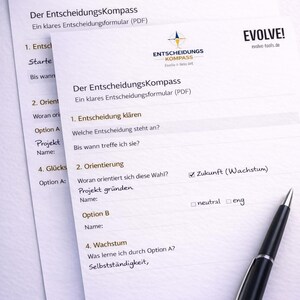 Pu&ograve; includere: Due fogli di lavoro bianchi per il processo decisionale con il testo "Der EntscheidungsKompass" e "EVOLVE!" sono visualizzati. Una penna nera &egrave; appoggiata sui fogli di lavoro. I fogli di lavoro hanno sezioni da compilare.