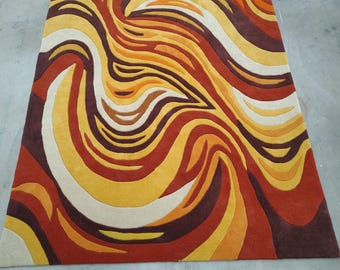 May include: A rectangular area rug featuring a dynamic, swirling pattern of organic, flowing shapes. The design incorporates a warm color palette consisting of deep chocolate brown, burnt orange, vibrant yellow, and creamy off-white tones.