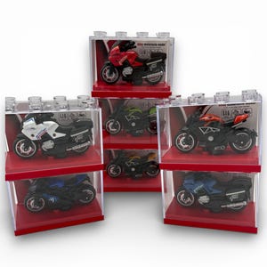 Könnte beinhalten: Eine Sammlung von Spielzeugmotorrädern in transparenten Kunststoff-Displayboxen. Die Motorräder sind in verschiedenen Farben erhältlich, darunter Rot, Weiß, Schwarz, Grün und Blau. Jedes Motorrad steht auf einem roten Sockel, und die Boxen sind gestapelt angeordnet.