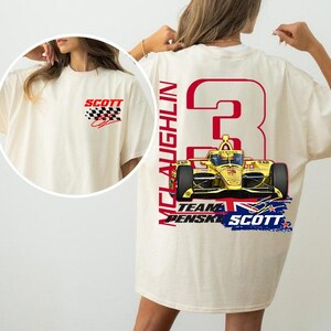 May include: Cream-coloured t-shirt with a racing car graphic on the back, displaying the number 3 and the name McLaughlin. The front of the shirt has the word "SCOTT" with a chequered flag design. The shirt has a casual, oversized fit.