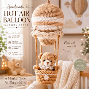 Op de afbeelding: Een gehaakte heteluchtballon decoratie voor de kinderkamer met een beige en wit gestreepte ballonkap met kleine strikjes, verbonden door vier gevlochten koorden aan een mandje met een kleine gehaakte teddybeer met een witte kanten kraag.