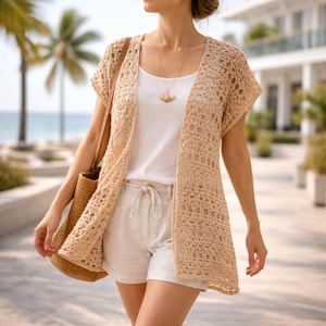 Puede incluir: Un cárdigan de crochet beige con frente abierto y mangas cortas. El cárdigan se usa sobre una camiseta sin mangas blanca y se combina con pantalones cortos de color claro. Se lleva un bolso tote tejido sobre el hombro. El fondo presenta palmeras y un edificio.