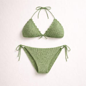 May include: A two-piece, green crochet bikini set. The top is a triangle style with scalloped edges and ties at the neck and back. The bottoms are a classic bikini cut with tie sides. The set is made of a soft, textured yarn.