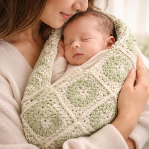 May include: A sleeping baby nestled in a handmade, light green and white crocheted baby carrier. The carrier features a square pattern design. The baby is held gently in someone's arms.