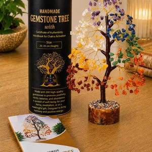 Peut inclure: Un arbre à pierres précieuses fait main avec des feuilles en cristal multicolores sur des branches en fil doré, un tronc marron et une base circulaire. Il est accompagné d'un tube de rangement cylindrique noir et d'un livret blanc, tous deux étiquetés "Handmade Gemstone Tree with Certificate of Authenticity Handbook for Chakra Activation" et "Size 26-28 cm (Height)".