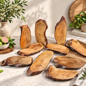 Könnte beinhalten: Eine Sammlung von Servierplatten und Schalen aus Naturholz mit unregelmäßigen Kanten und sichtbarer Holzmaserung. Diese Holzstücke variieren in Form und Größe und zeigen die organische Textur sowie die warmen Brauntöne des Holzes.