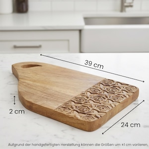 Può includere: Tagliere rettangolare in legno chiaro, lungo 39 cm, largo 24 cm e spesso 2 cm. Presenta un motivo floreale intagliato e un manico.
