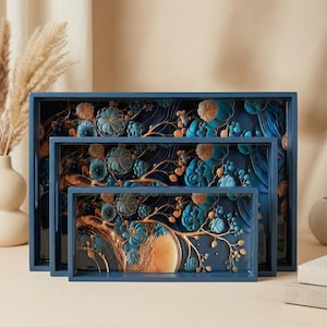 May include: Three nested decorative trays in varying sizes. The trays are navy blue with a floral design in teal and gold. The floral design is raised, creating a 3D effect. The trays have a rectangular shape.